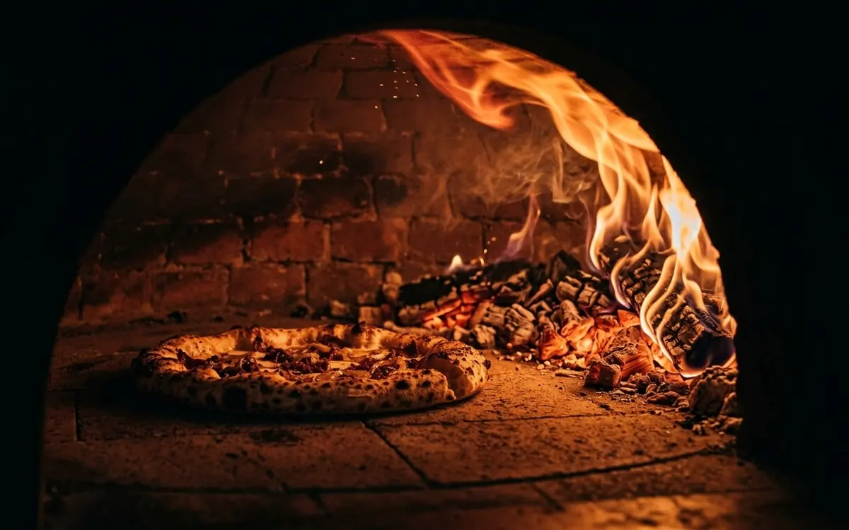 Pizza assando no forno a lenha com a chama viva